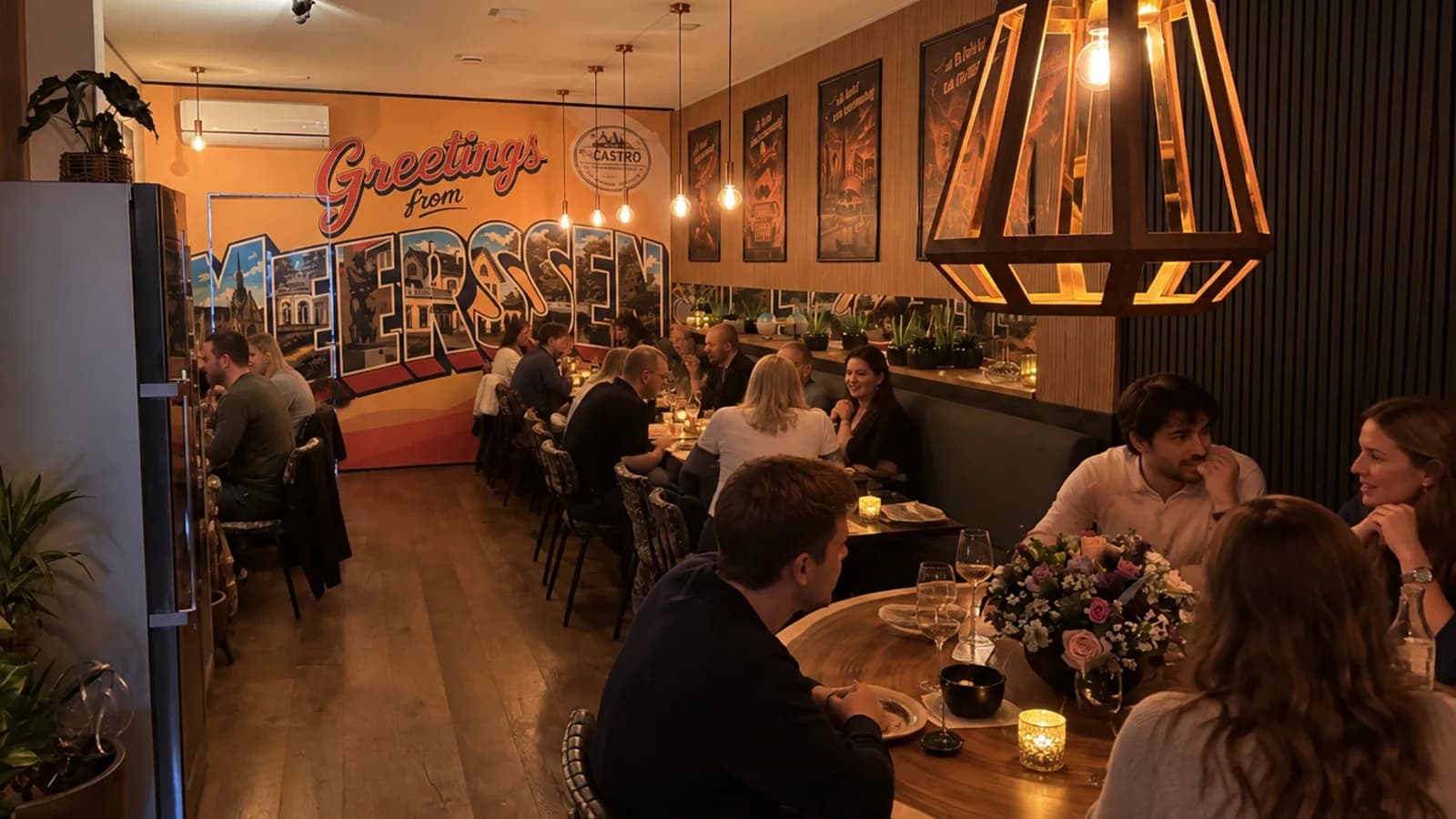 De zaal van By Castro in Meerssen op een volle avond, met de Greetings from Meerssen-muurschildering en de bestemmingsposters aan de wand